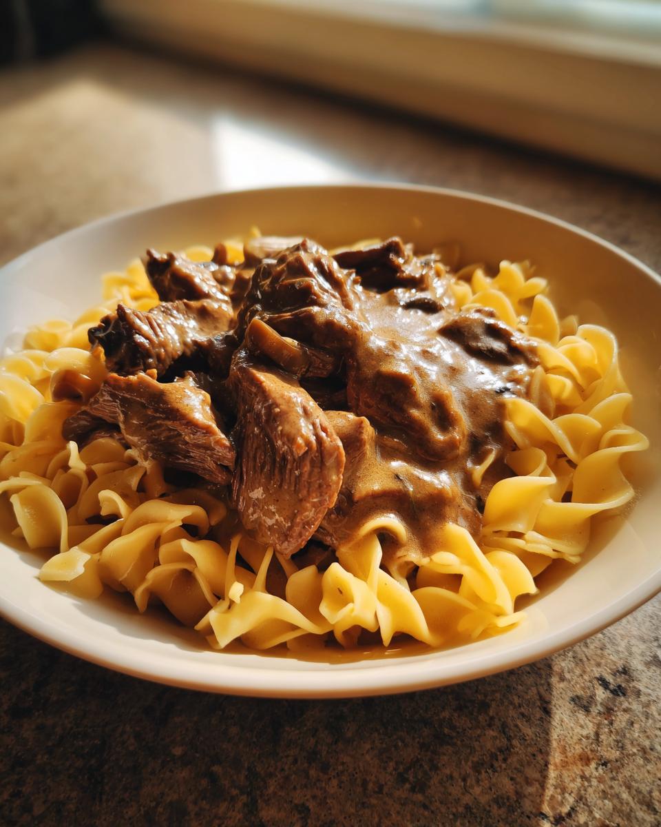 A close-up of a bowl featuring tender beef pieces and creamy sauce from the ultimate beef stroganoff served over wide egg noodles.