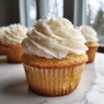 A close-up of a perfectly baked vanilla cupcake from scratch topped with a swirl of white buttercream frosting.