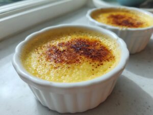 Close-up of two bright yellow vanilla custard cups topped with perfectly caramelized, dark brown sugar crusts.