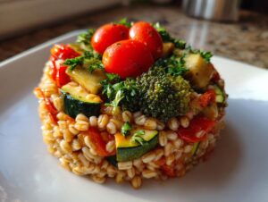 A perfectly molded portion of vegan vegetable barley salad featuring zucchini, broccoli, and cherry tomatoes.