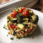 A perfectly molded serving of vegan vegetable barley salad featuring barley, zucchini, broccoli, and topped with roasted cherry tomatoes.