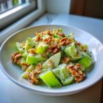 A vibrant bowl of celery salad featuring crisp celery chunks, apple slices, walnuts, and a creamy dressing.
