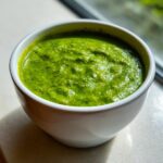 Close-up of a small white bowl filled with thick, vibrant green enchilada sauce, ready for use.