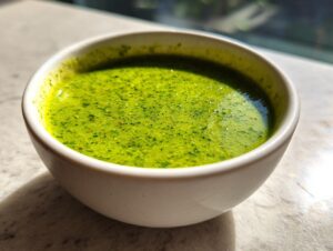 Close-up of vibrant green enchilada sauce, slightly textured, served in a small white bowl.