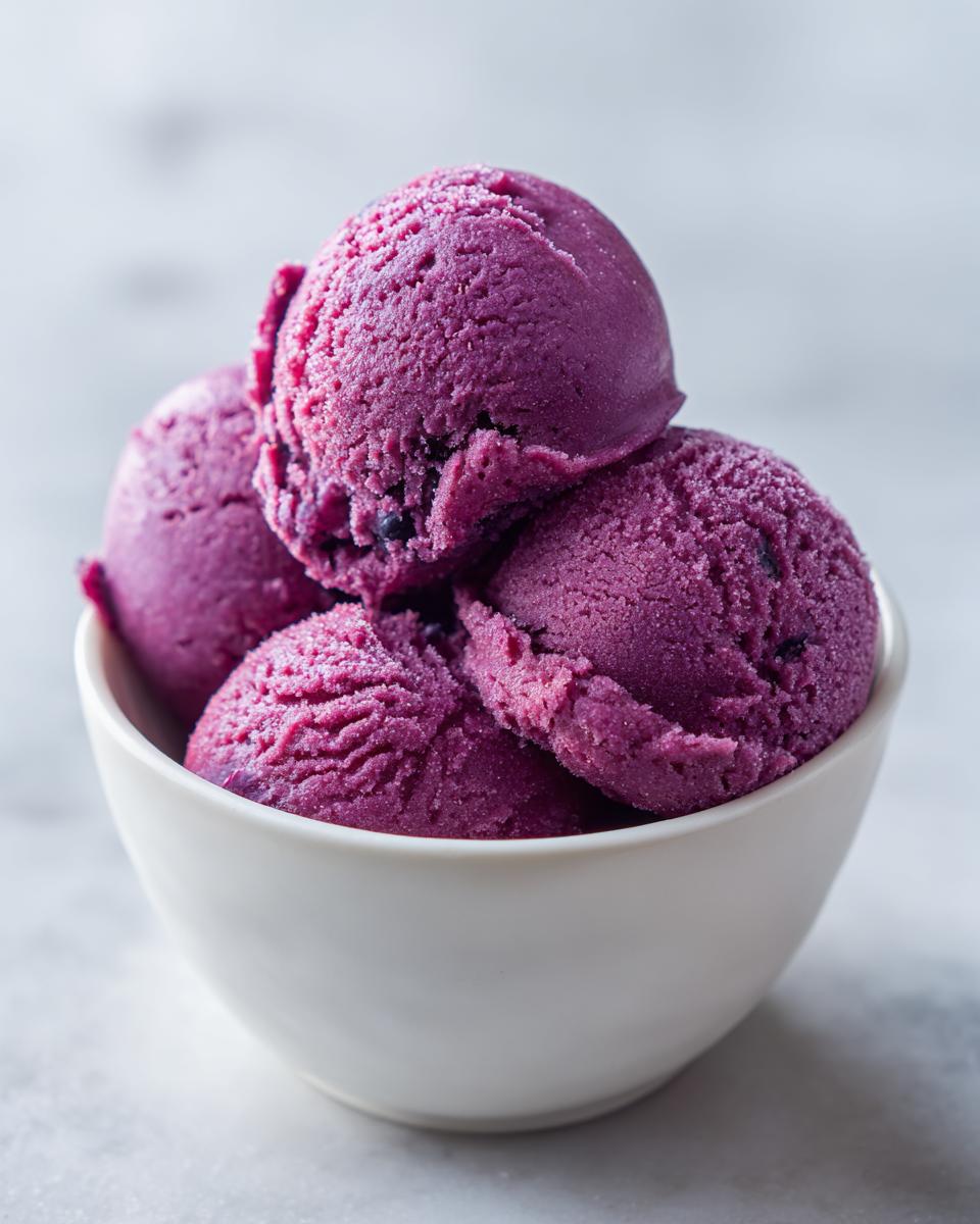 Close-up of four scoops of vibrant purple summer sherbet served in a small white bowl.