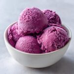 Close-up of several scoops of vibrant purple summer sherbet dusted with frost in a white bowl.