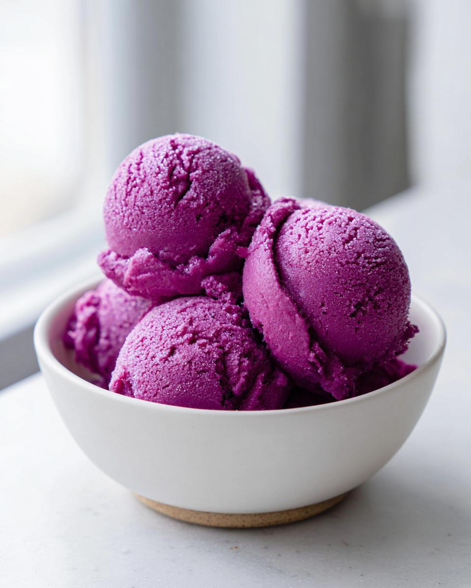 Four scoops of bright purple summer sherbet piled high in a white bowl.