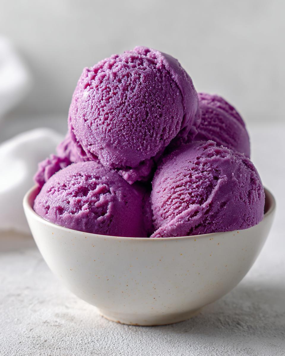 Close-up of several scoops of bright purple summer sherbet served in a small, speckled white bowl.