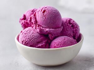 Close-up of several scoops of bright magenta summer sherbet, slightly frosted, served in a small white bowl.