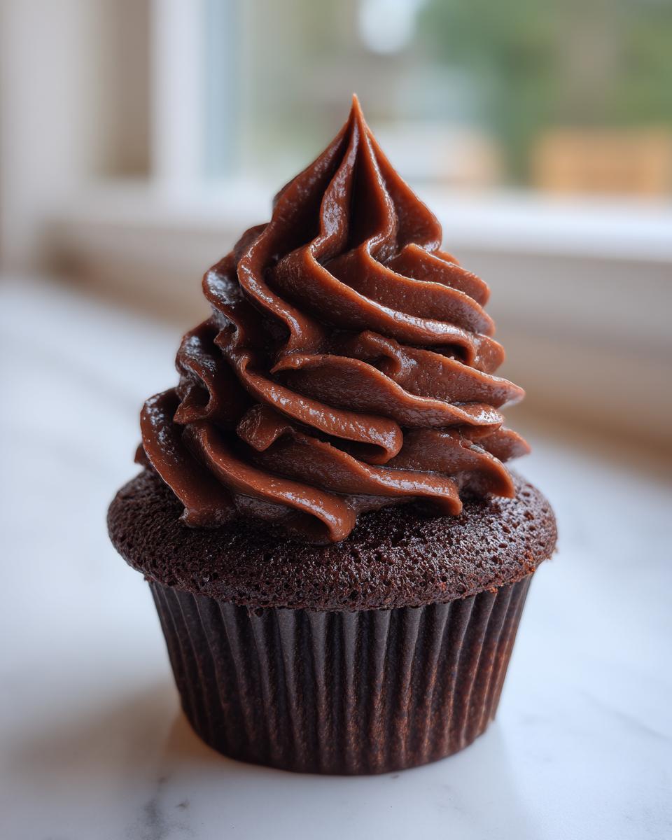 A single, decadent chocolate cupcake topped with a tall swirl of rich whipped chocolate ganache.