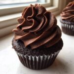 A close-up of a decadent chocolate cupcake topped with perfectly piped whipped chocolate ganache frosting.