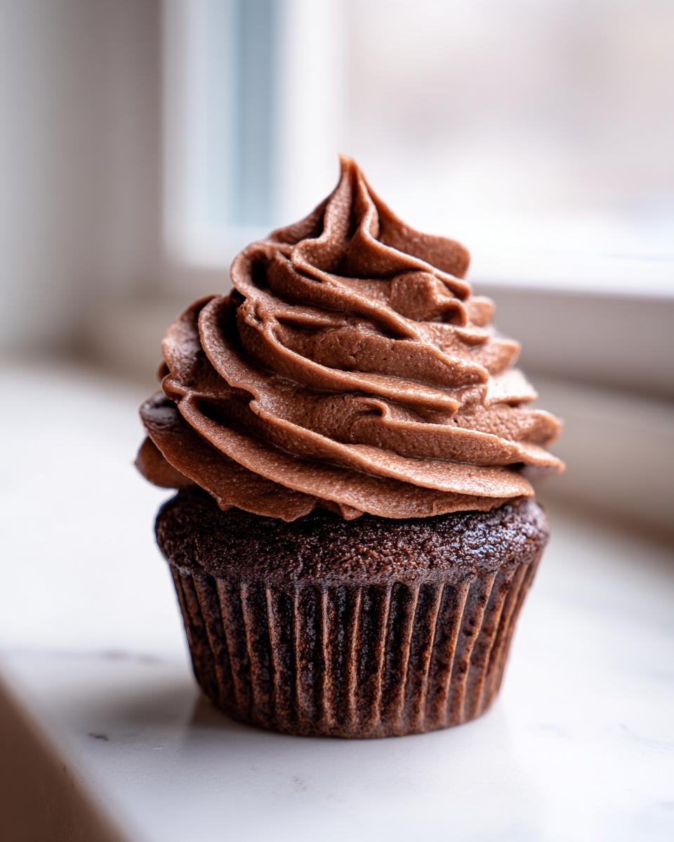 A single, rich chocolate cupcake topped with a tall swirl of whipped chocolate ganache frosting.