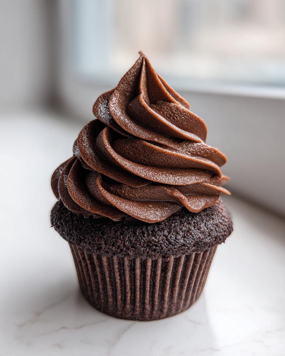 A single, rich chocolate cupcake topped with a tall swirl of whipped chocolate ganache frosting.