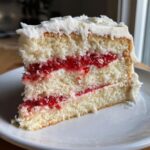 Close-up of a moist slice of white chocolate raspberry layer cake showing three layers of white cake and two layers of bright red raspberry filling.