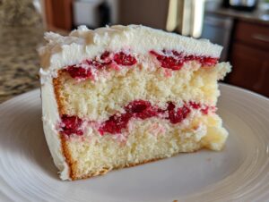 A close-up slice of white chocolate raspberry layer cake showing three layers of moist cake, raspberry filling, and white frosting.