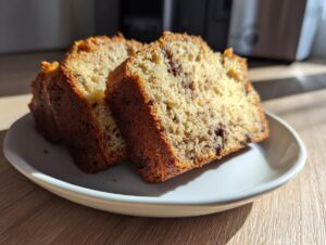 Two thick slices of moist world’s best banana bread, studded with chocolate chips, on a white plate.