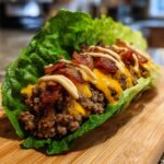 A close-up of a low-carb bacon cheeseburger wrap made with ground beef, melted cheese, bacon, and sauce inside a crisp lettuce leaf.