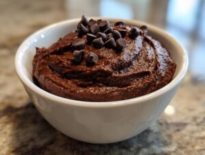 A close-up of rich, dark brown chocolate dessert hummus served in a white bowl and topped with chocolate chips.