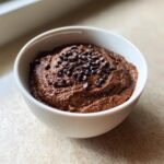 A close-up of rich, dark Chocolate dessert hummus served in a white bowl and topped with mini chocolate chips.