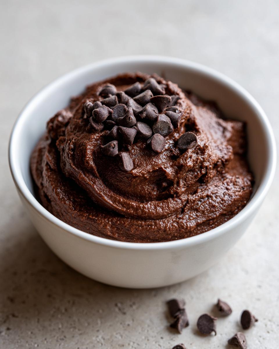 A white bowl filled with rich, dark Chocolate dessert hummus, topped with chocolate chips.