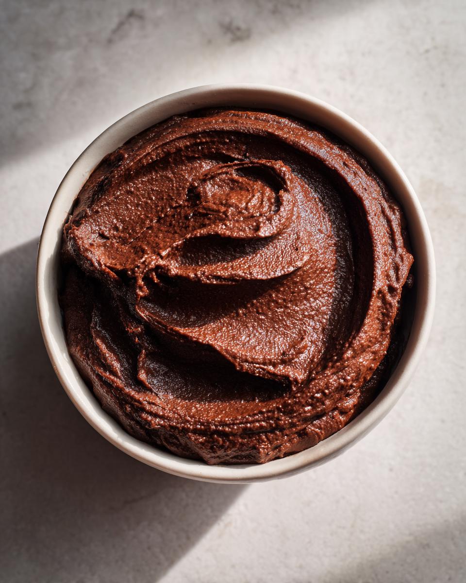 Overhead view of rich, dark chocolate dessert hummus swirled in a small white bowl.