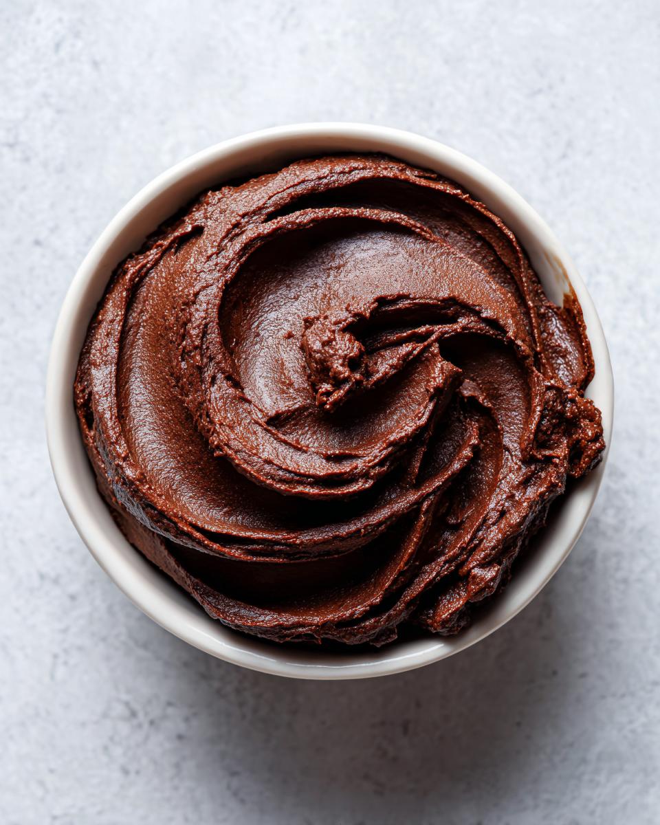 Overhead shot of rich, dark chocolate dessert hummus swirled beautifully in a small white bowl.