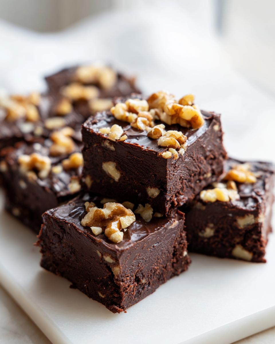 Close-up of decadent chocolate walnut fudge squares topped with chopped walnuts.