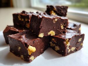 A stack of rich, dark chocolate walnut fudge squares, showing visible chunks of walnuts throughout the dense confection.