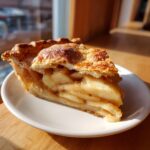 A close-up of a perfect slice of Classic apple pie showing thick apple filling and a flaky, sugared crust.