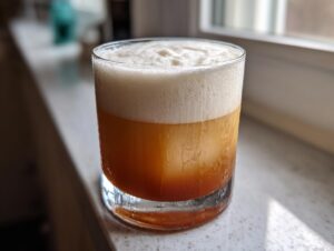 A close-up of a freshly made Classic whiskey sour cocktail with a thick, creamy layer of foam.