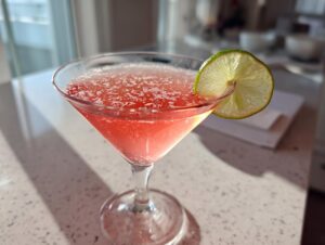 A vibrant pink Cosmopolitan cocktail served in a martini glass, garnished with a bright lime wheel.