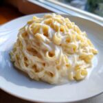 A close-up of a generous serving of rich, creamy fettuccine alfredo pasta piled high on a white plate.
