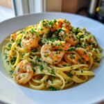 A close-up of a white bowl filled with Garlic lemon shrimp pasta, topped with plump shrimp and fresh green herbs.