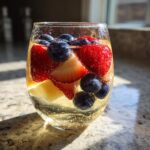 Close-up of a glass filled with sparkling Moscato sangria, loaded with fresh strawberries and blueberries.