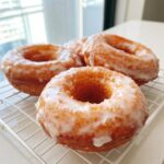 Close-up of several golden brown glazed yeast donuts resting on a white wire cooling rack.