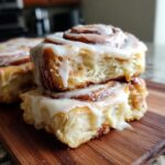 Two stacked, gooey homemade cinnamon rolls dripping with white icing, showing the soft interior texture.