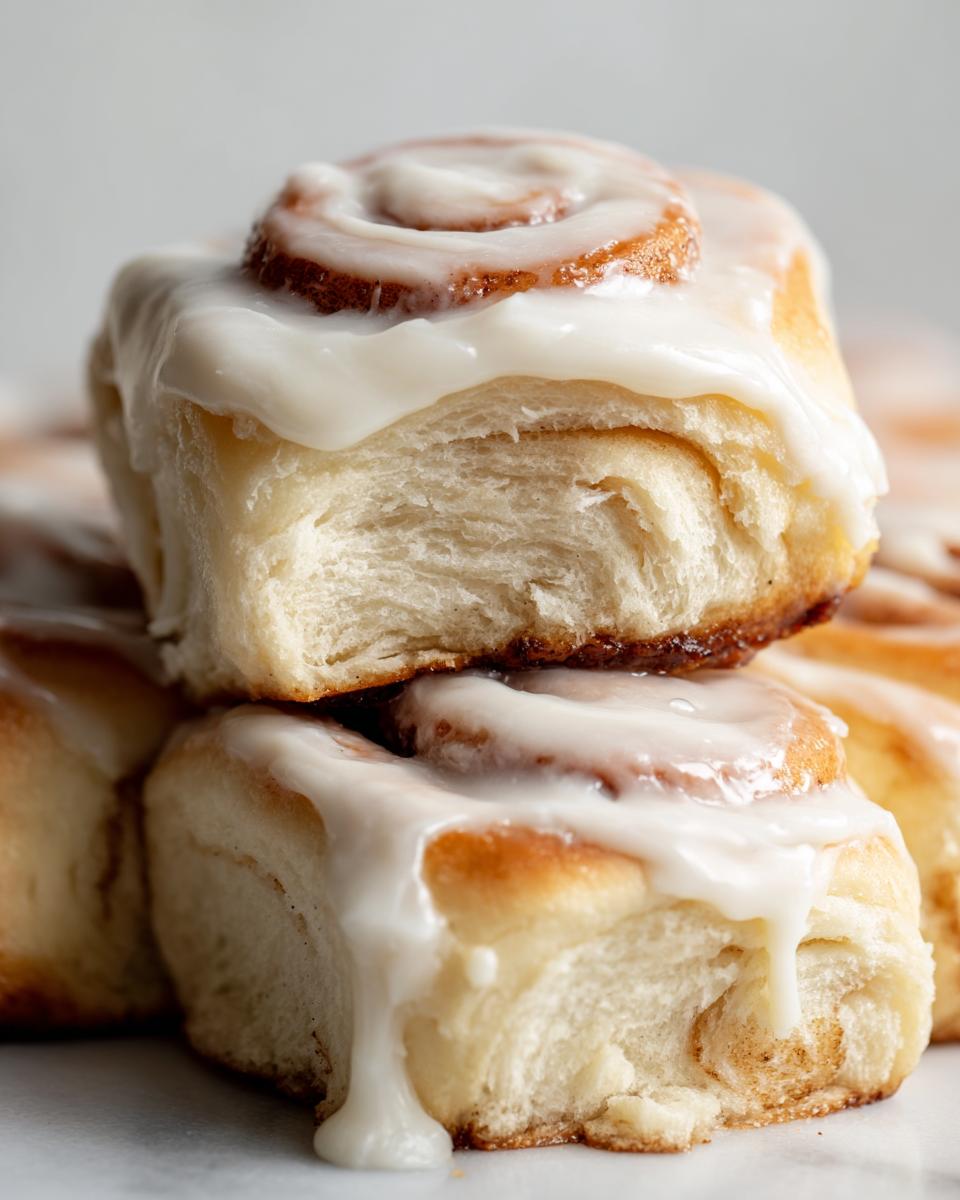 Close-up of two fluffy Homemade Cinnamon Rolls stacked, dripping with thick white cream cheese icing.