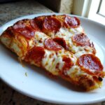 Close-up of two thick slices of homemade pepperoni pizza featuring bubbly, melted mozzarella cheese and crispy pepperoni.