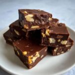 A stack of rich, dark chocolate Maple walnut fudge squares studded with visible walnut pieces, served on a white plate.