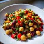 Close-up of a vibrant Mediterranean bean salad featuring chickpeas, kidney beans, diced red peppers, and fresh parsley.