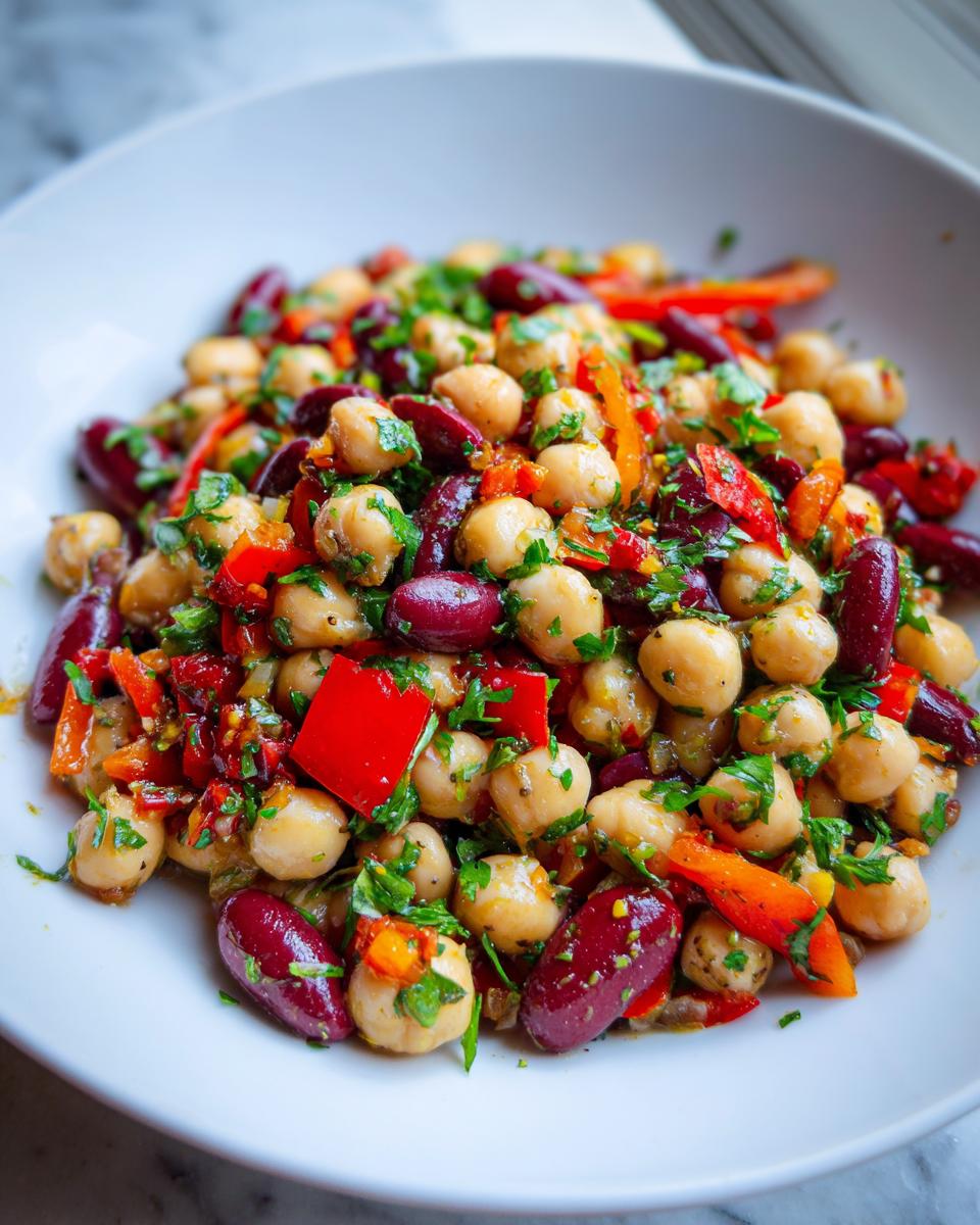 Close-up of a vibrant Mediterranean bean salad featuring chickpeas, dark red kidney beans, chopped red peppers, and fresh parsley.