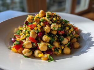 A mound of colorful Mediterranean bean salad featuring chickpeas, kidney beans, yellow peppers, and fresh parsley on a white plate.