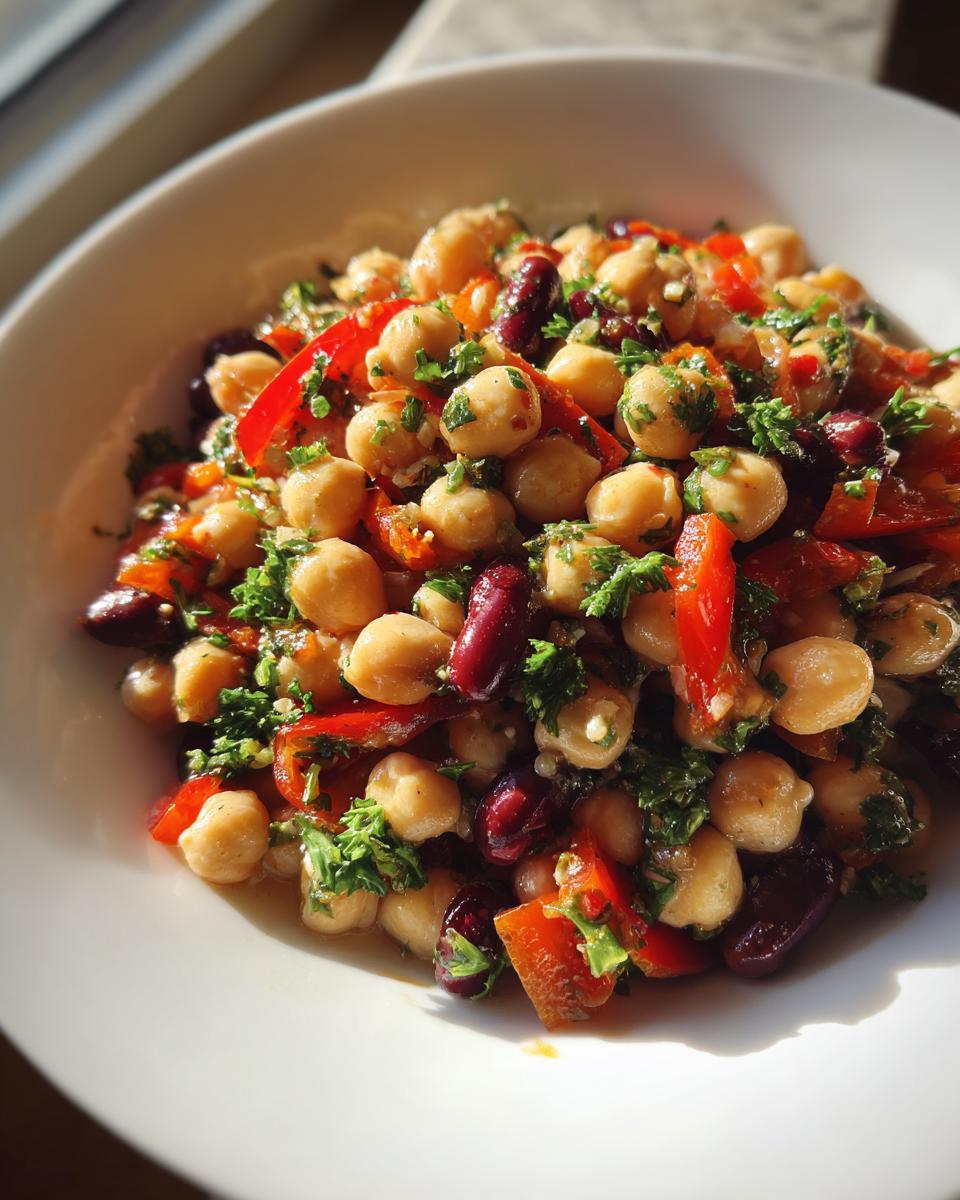 Close-up of a bright Mediterranean bean salad featuring chickpeas, kidney beans, red peppers, and fresh parsley.