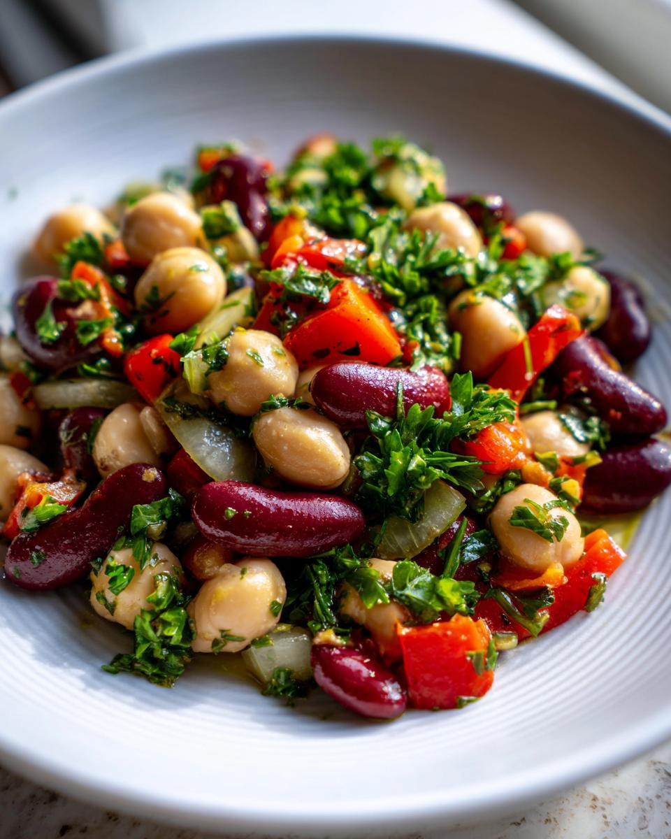Close-up of a vibrant Mediterranean bean salad featuring chickpeas, kidney beans, red peppers, onions, and fresh parsley.