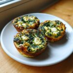 Three perfectly baked mini spinach quiche bites with visible feta cheese on a white plate.