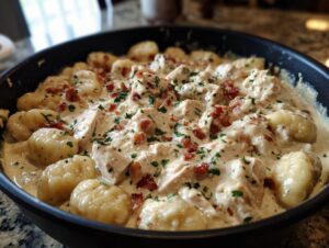Close-up of one pan creamy gnocchi mixed with chicken pieces, bacon bits, and fresh parsley in a rich white sauce.