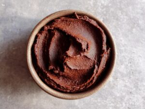 Overhead view of rich, dark chocolate dessert hummus swirled in a small, rustic brown bowl.