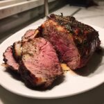 A juicy roast leg of lamb, perfectly medium-rare, sliced and seasoned with herbs on a white plate.