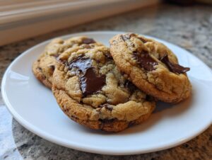 Three perfectly baked soft chewy chocolate chip cookies with melted chocolate chunks resting on a white plate.
