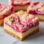 A square slice of swirled rhubarb bars showing a graham cracker crust, creamy base, and bright pink rhubarb swirl topping.